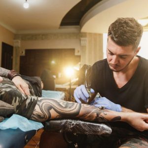 professional-tattooer-artist-doing-tattoo-arm-young-man-by-machine-with-black-ink